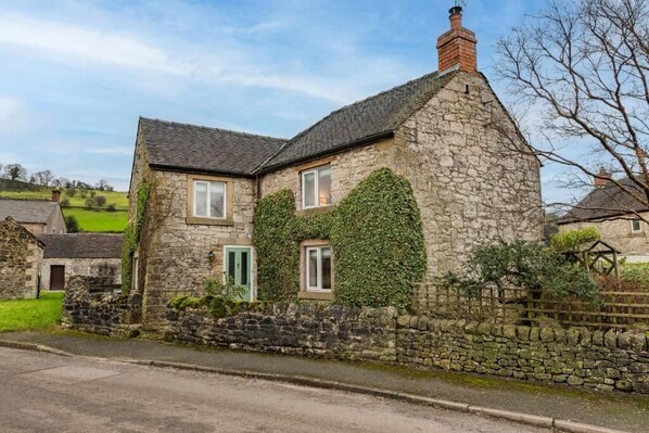 A stone house with ivy-covered walls, a chimney, and a stone wall surrounding the property.