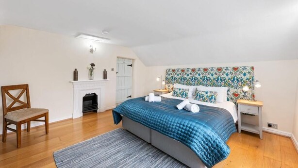 A bedroom with a bed, a chair, a fireplace, and a patterned headboard. - Host & Stay | Ivy Farm House - Wetton (Ashbourne)