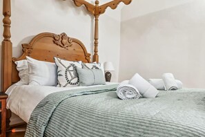 Una cama bien hecha con colcha verde, almohadas blancas y toallas enrolladas.