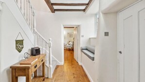 Un pasillo estrecho con suelo de madera, un banco de madera, una puerta blanca y una escalera con barandillas blancas.