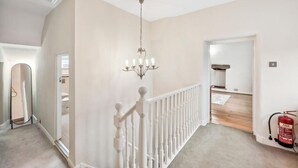A hallway with a white railing, a chandelier, and a fire extinguisher. - Host & Stay | Ivy Farm House - Wetton (Ashbourne)