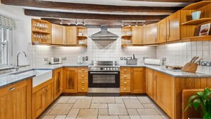 A kitchen with wooden cabinets, a stainless steel stove, and a tiled backsplash. - Host & Stay | Ivy Farm House - Wetton (Ashbourne)