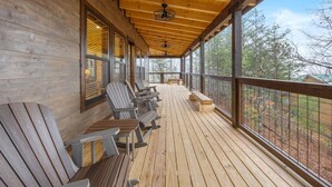 En täckt träveranda med Adirondack-stolar och en bänk, med utsikt över ett skogsområde.