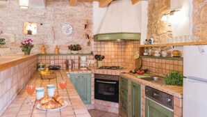 A kitchen with stone walls, wooden beams, a tiled backsplash, and a variety of kitchen appliances and utensils.