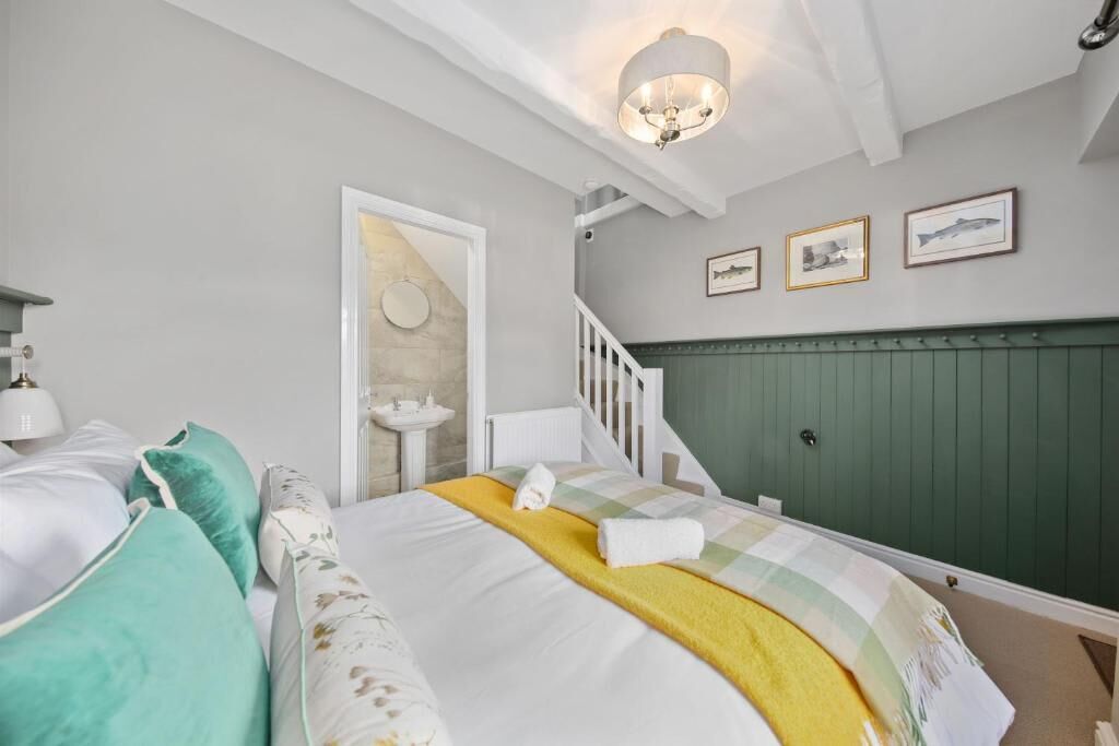 A bedroom with a bed, a nightstand, a dresser, a window, and a staircase.