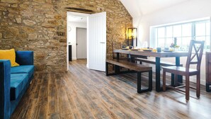 A room with a stone wall, a dining table with chairs, a blue sofa, and a window with a view. - Host & Stay | Staffordshire Knot (Sheen)