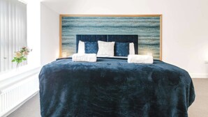 Een slaapkamer met een groot bed, een hoofdeinde en een kunstwerk aan de muur.