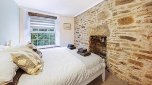 A bedroom with a stone wall, a bed with patterned pillows, a window with blinds, and a fireplace. - Host & Stay | Batemill Cottage (Birch Vale)