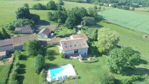 Vista aérea de uma propriedade rural com vários edifícios, piscina e campos verdes ao redor.