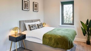 Un dormitorio moderno con cama, mesitas de noche, una ventana y una planta en maceta.