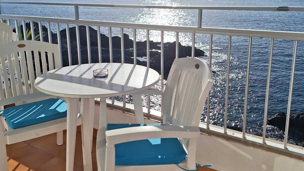 Une terrasse avec une table et des chaises blanches, une vue sur la mer et une balustrade.