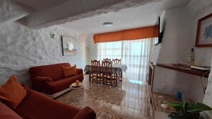 Un salon comprenant un canapé, une table à manger avec des chaises, un téléviseur fixé au mur et un sol à motifs.