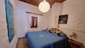 Une chambre avec un grand lit, un plafond en bois, une fenêtre avec des rideaux, un tableau au mur et une table de chevet avec une lampe.