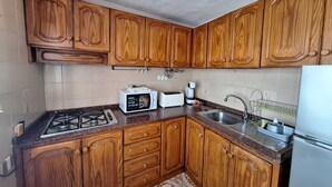Une cuisine avec des meubles de rangement en bois, une cuisinière à gaz, un four à micro-ondes, un grille-pain, un évier et un réfrigérateur.