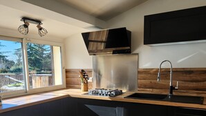 A modern kitchen with a large island, stainless steel appliances, and a wooden backsplash. - Villa with pool near Uzès (Saint-Laurent-la-Vernède)
