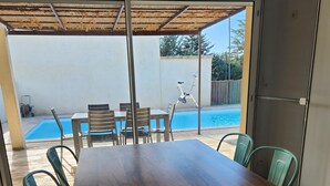 A wooden dining table with chairs, a pool, and a covered area with a ceiling. - Villa with pool near Uzès (Saint-Laurent-la-Vernède)