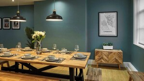A dining area with a long wooden table set for a meal, two pendant lights, a framed map on the wall, and a herringbone-patterned wooden cabinet. - Host & Stay | The Falkner Quarters I and II (Merseyside)