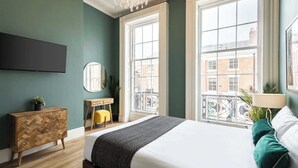 A bedroom with a bed, a dresser, a mirror, and a window with a view of buildings. - Host & Stay | The Falkner Quarters I and II (Merseyside)
