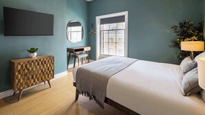 Een slaapkamer met een bed, een dressoir, een bureau, een spiegel, een televisie, een raam en een lamp.