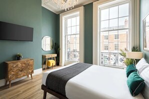 A bedroom with a bed, a dresser, a mirror, and a window with a view of buildings.