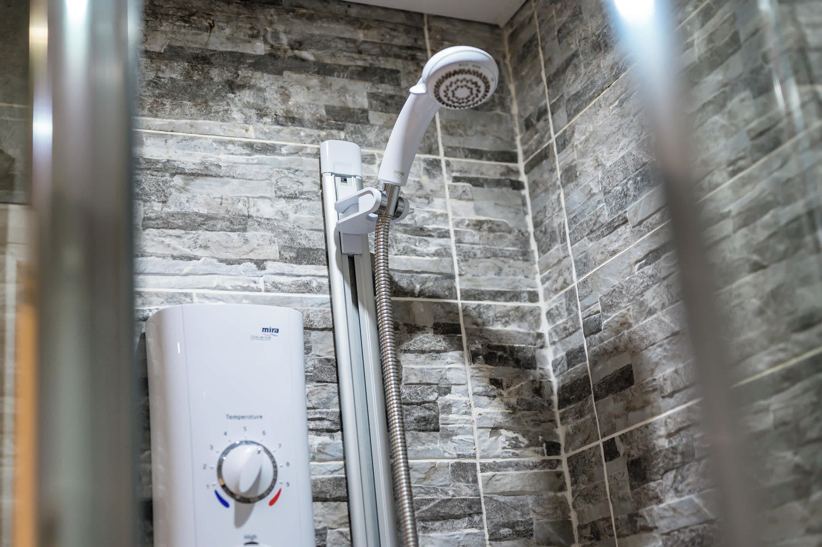 A shower with a stone wall backdrop and a control panel with a temperature dial.