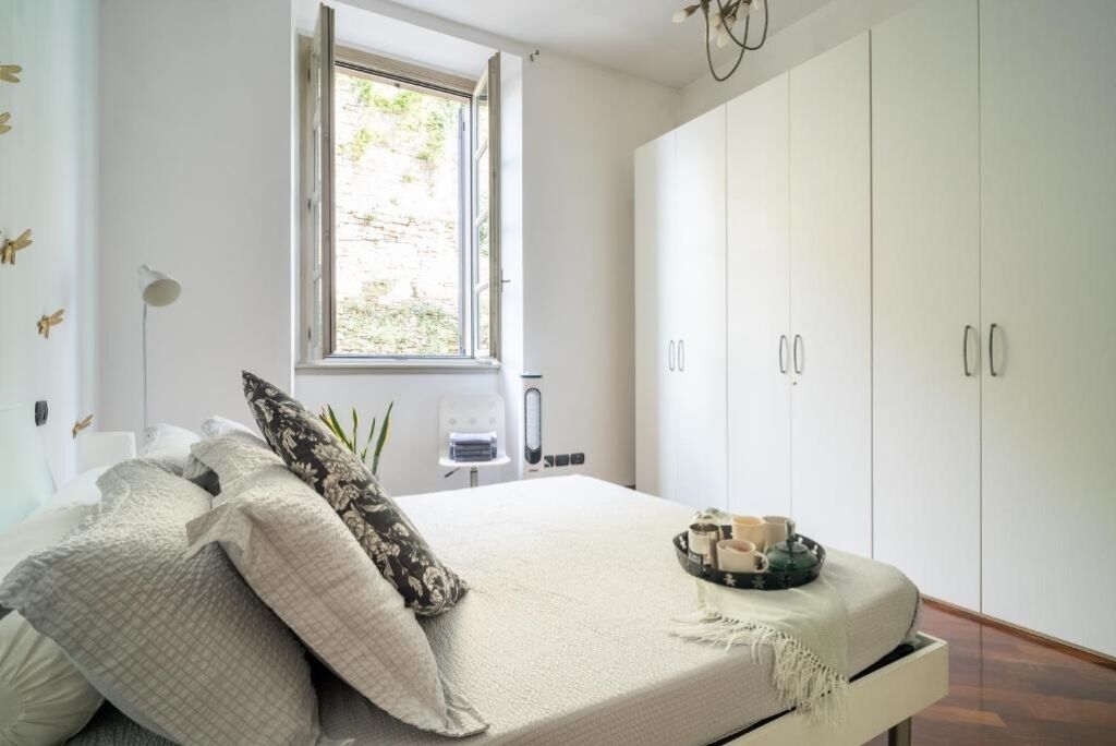 A bedroom with a bed, a window, a wardrobe, and a bedside table with a tray.