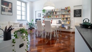 Una sala de estar moderna con un sofá blanco, una mesa de comedor y sillas, una estantería y un ventanal grande.