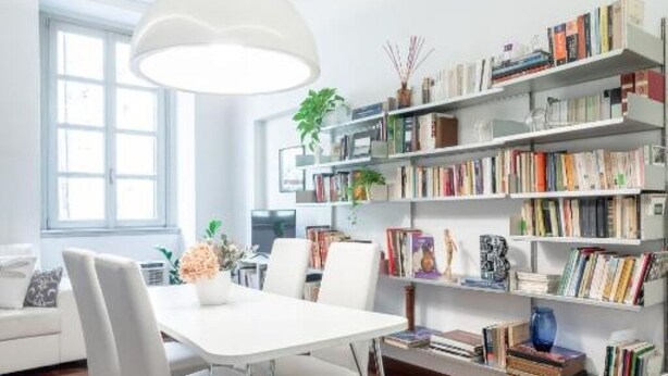 Una sala de estar moderna con un sofá blanco, una mesa de comedor y una estantería llena de libros.