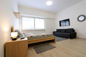 Un dormitorio con cama, mesita de noche, lámpara y sofá negro.