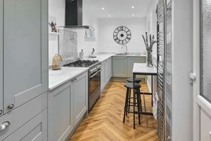 A modern kitchen with grey cabinets, a white countertop, a gas stove, and a wooden herringbone floor. - Host & Stay  | Railway Cottages (Liverpool)