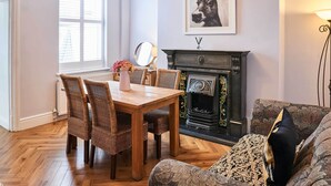 A dining area with a wooden table and wicker chairs, a fireplace with a decorative mantle, and a framed picture on the wall.