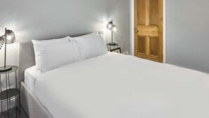 A neatly made bed with white linens, two bedside tables with lamps, and a wooden door.