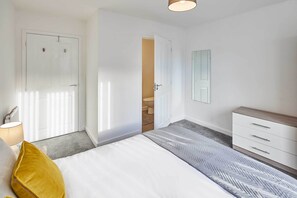 Quarto com cama, mesa de cabeceira, cômoda, espelho e porta para um banheiro.