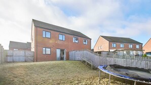 Ett bostadsområde med ett hus byggt av tegel, ett trästaket och en studsmatta på gården.