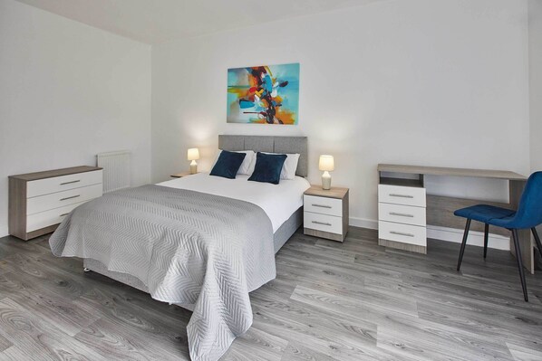 A modern bedroom with a bed, bedside tables, a desk, and a chair.