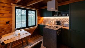 A compact kitchen with wooden walls, a window with blinds, a sink, a countertop, and green cabinets.