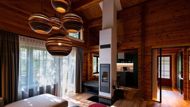 A log cabin interior with a cozy living area, a fireplace, and a kitchen visible through an open door.