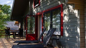 A deck with two lounge chairs, a table, and chairs, and a red door with windows.