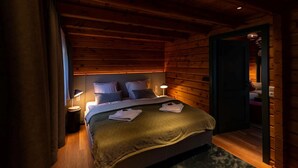 A cozy wooden cabin bedroom with a bed, two bedside lamps, and a nightstand.