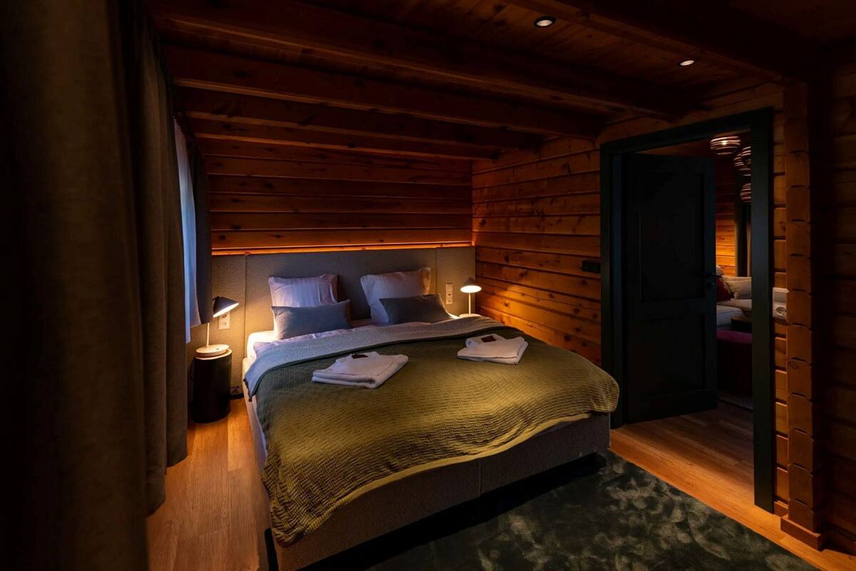 Un dormitorio acogedor de cabaña de madera con una cama, dos lámparas de noche y una mesita de noche.