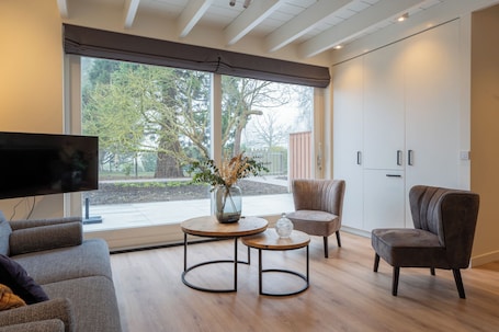 A modern living room with a flat-screen TV, two round tables, a sofa, and a chair.