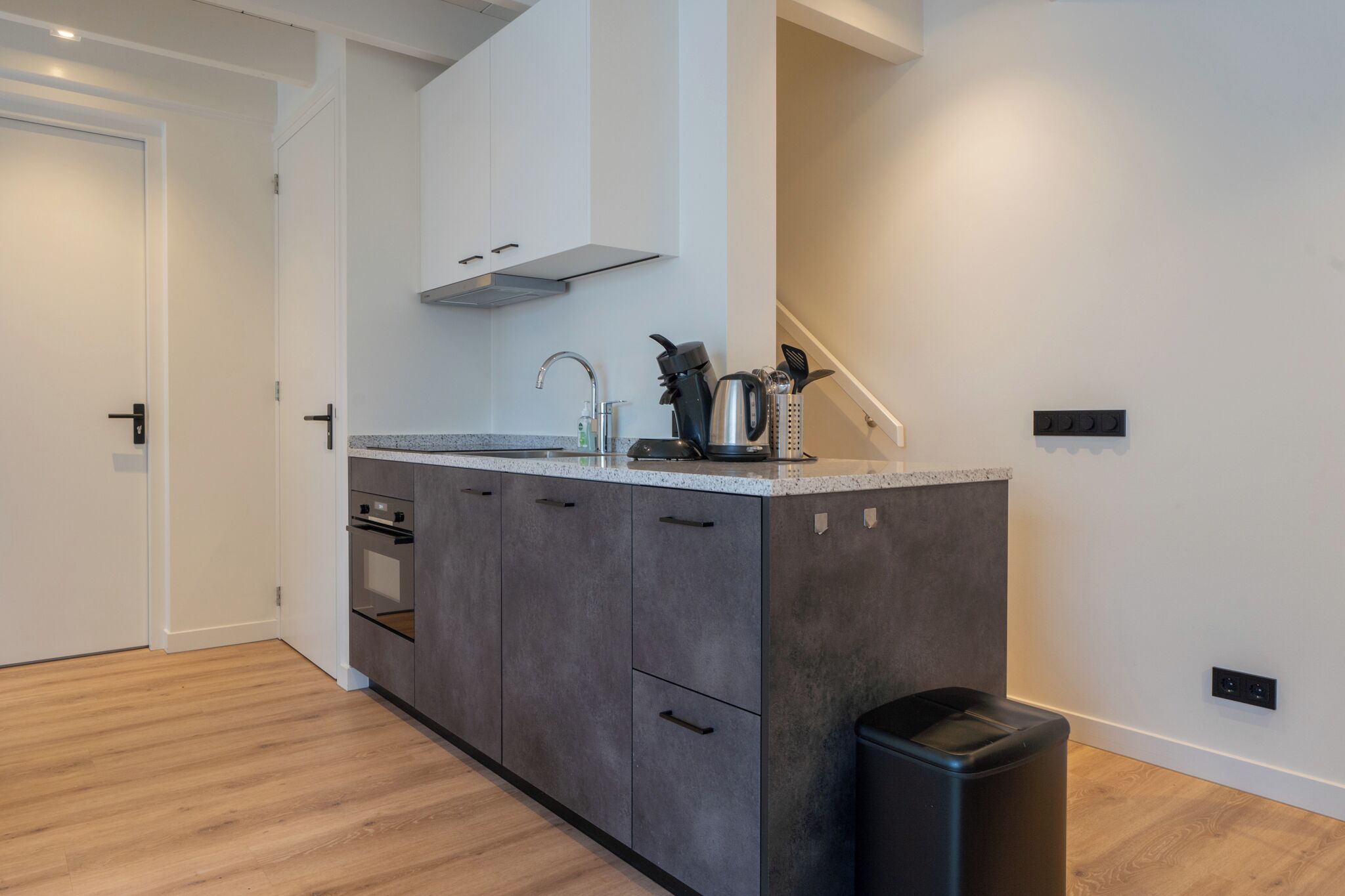 Une cuisine moderne avec des meubles gris, un évier en acier inoxydable et une poubelle noire.
