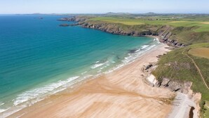 Un paysage côtier avec une plage de sable, des falaises rocheuses et une vue dégagée sur l’océan.