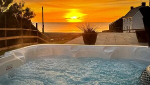 Un jacuzzi avec vue sur le coucher de soleil sur l’océan, une clôture en bois et un bâtiment en arrière-plan.