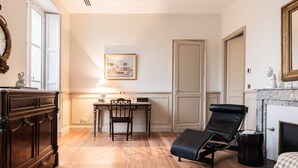 A room with a wooden floor, a desk with a chair, a black leather chair, a fireplace, and a door.