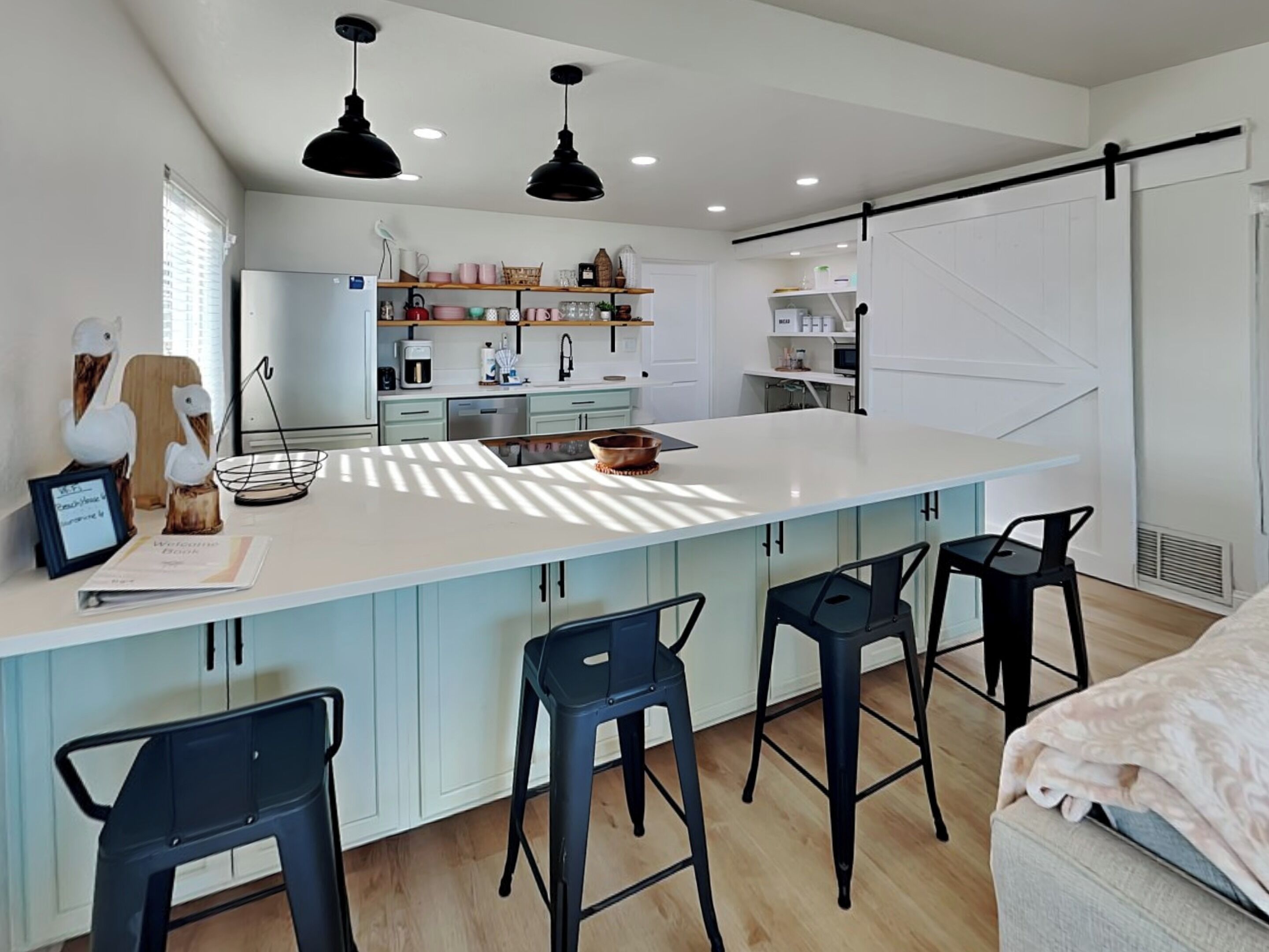 A modern kitchen with a large island, bar stools, pendant lighting, and a sliding barn door.