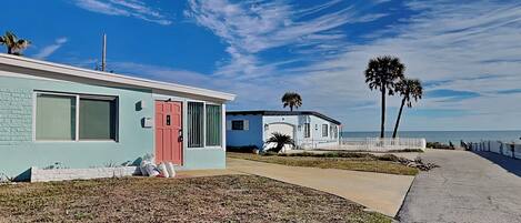 A coastal building with a light blue exterior, a red door, and a white fence.
