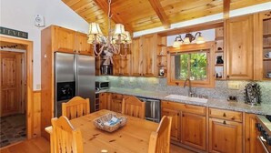 Cocina tipo cabaña de madera con una isla central, electrodomésticos de acero inoxidable y una ventana con vistas a la vegetación.