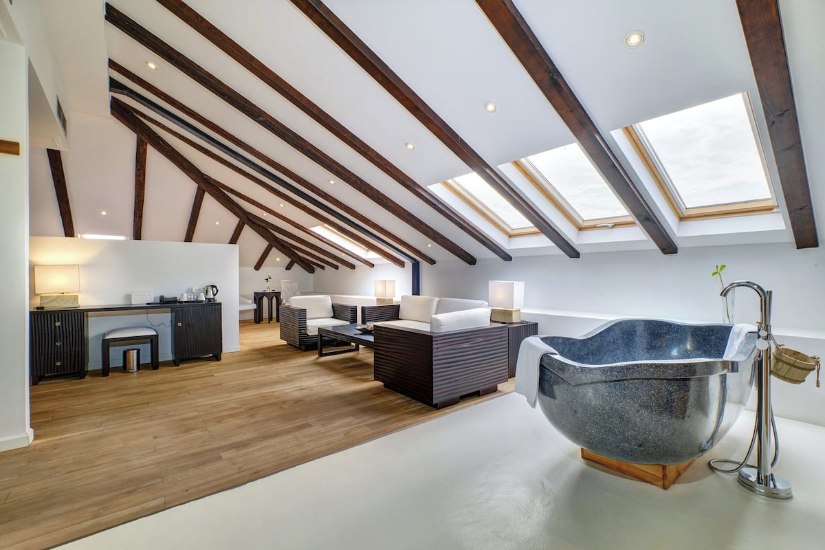 A spacious loft with a high ceiling, skylights, a large stone bathtub, and a cozy seating area.