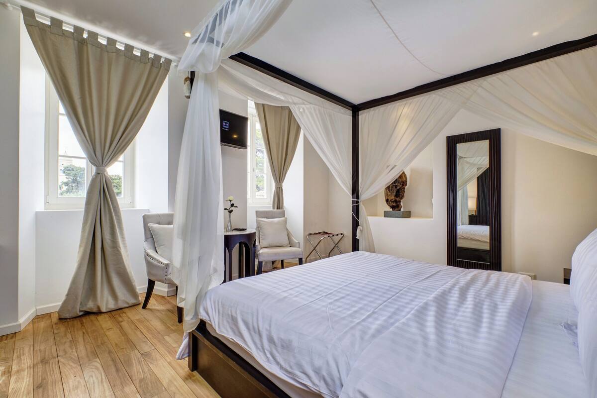 A bedroom with a large bed, a chair, a small table, and a mirror.
